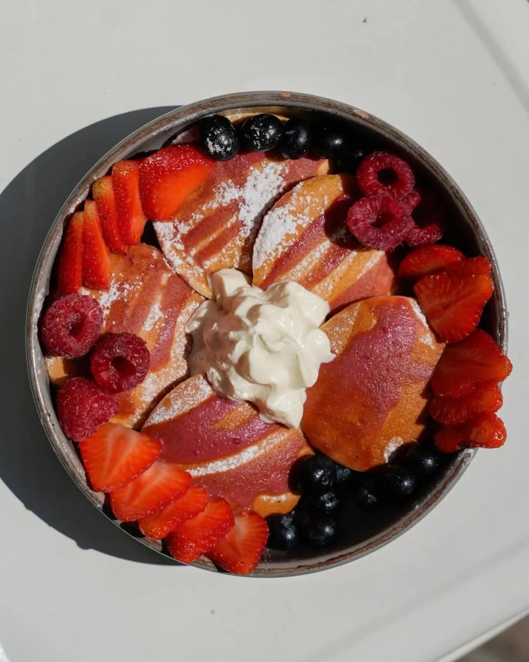 Red berry pancakes with strawberries, raspberries, blueberries and cream