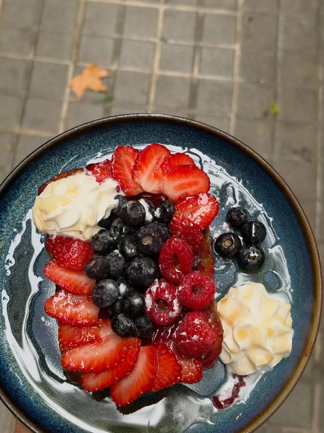 A thick toast covered in strawberries, blueberries and raspberries, with cream